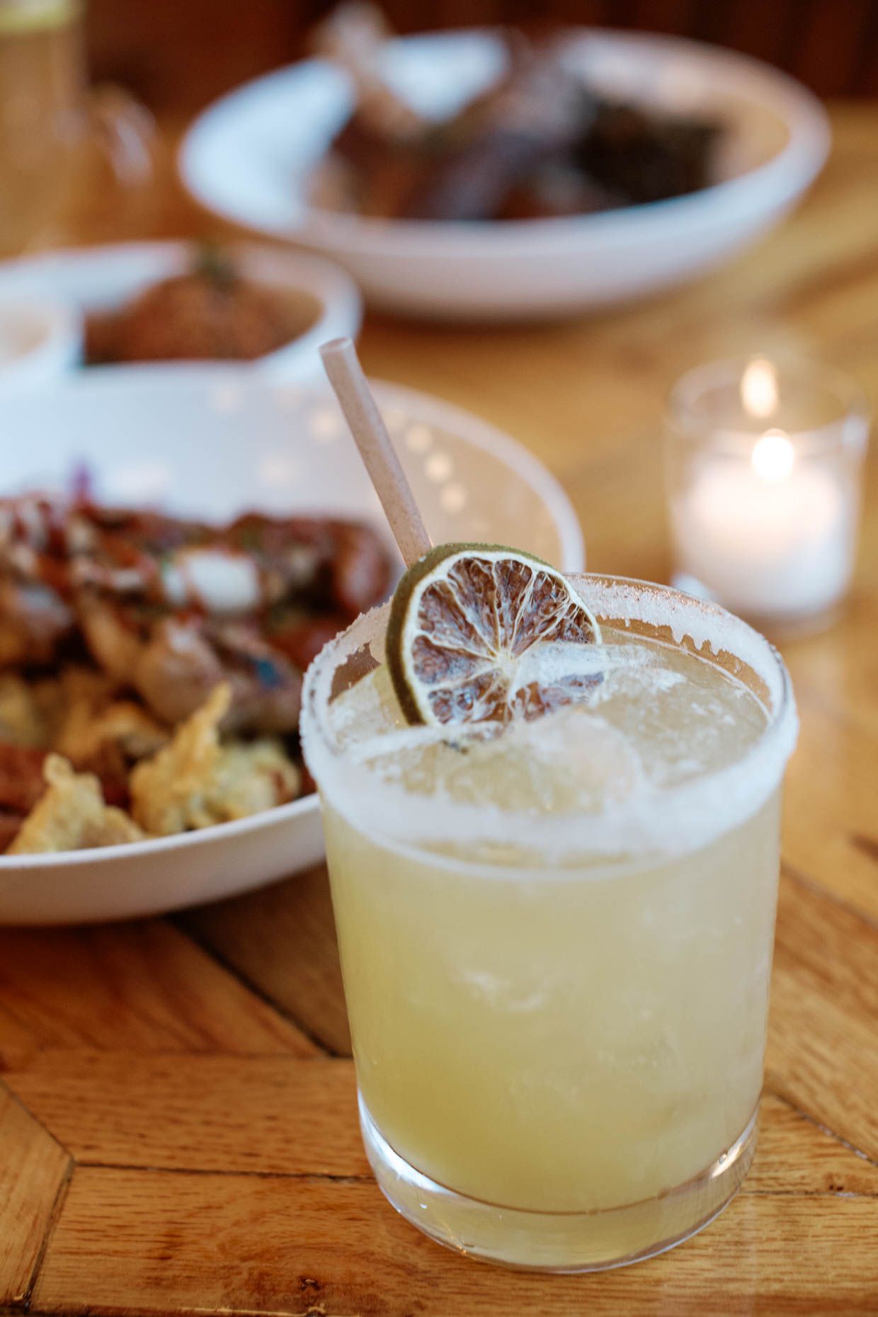 A frothy margarita garnished with a dried lime slice and straw served on a wooden table.