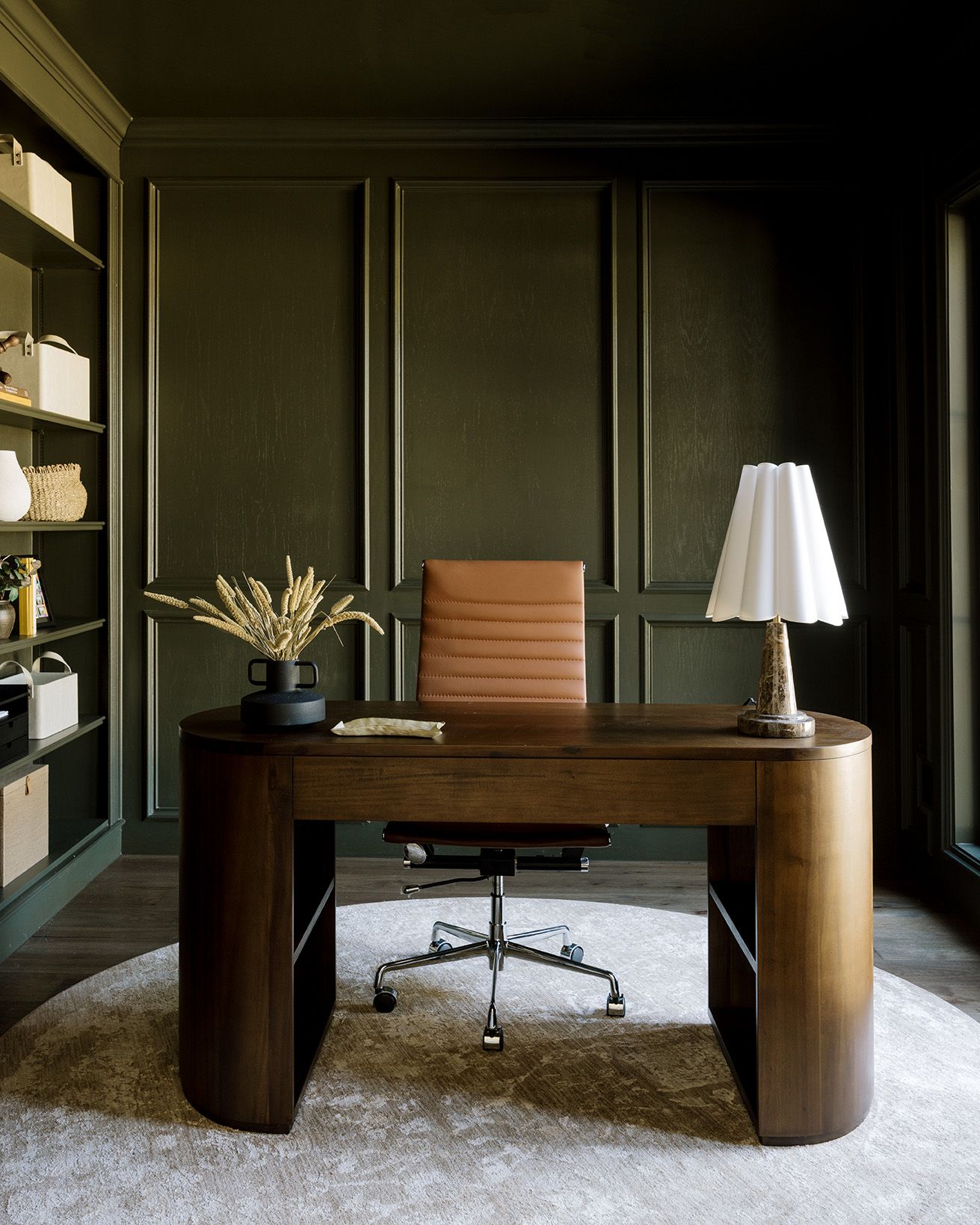 Sophisticated home office with dark olive green walls, curved walnut desk, and leather chair.