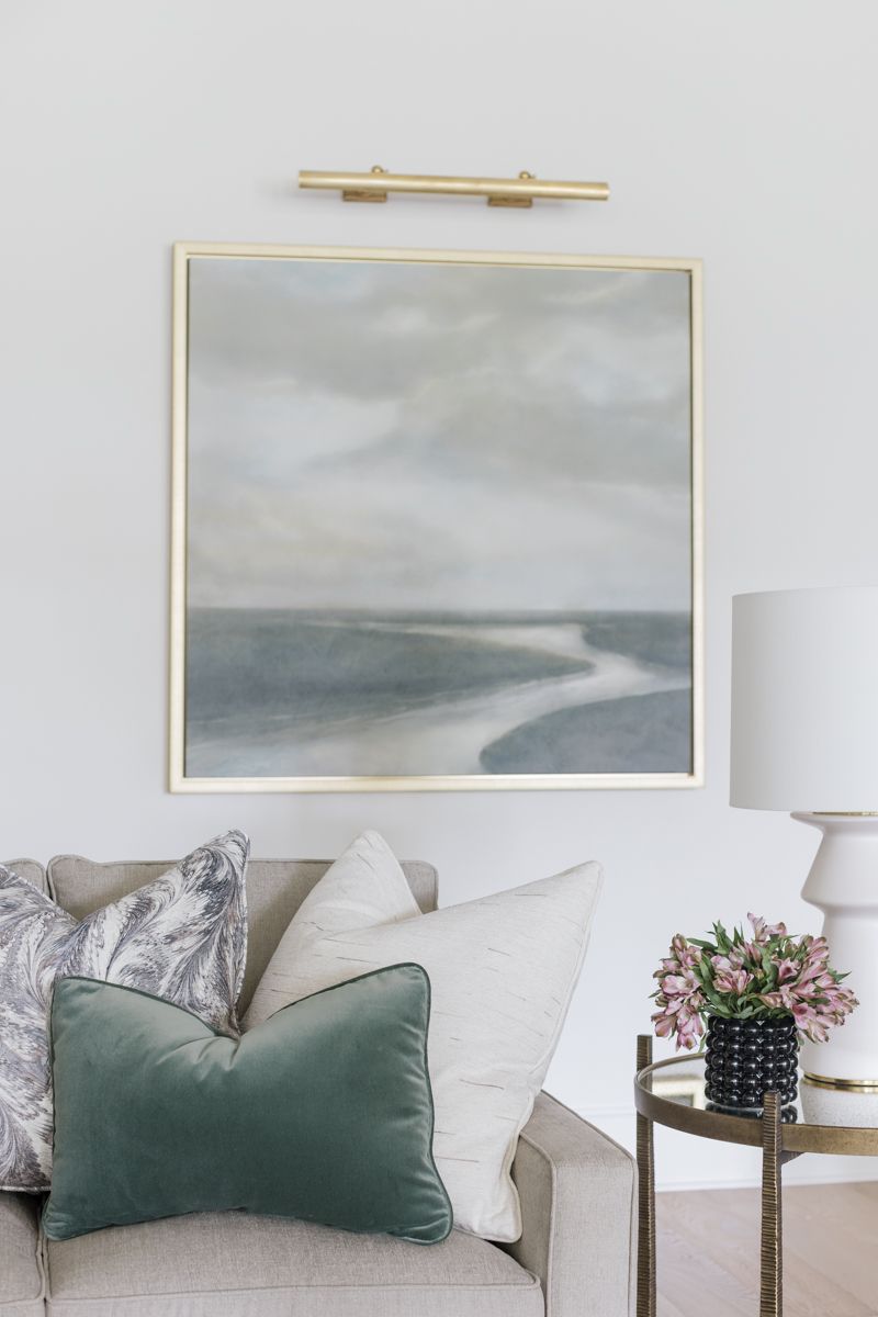 Coastal abstract painting in gold frame above neutral sofa with green velvet accent pillow.