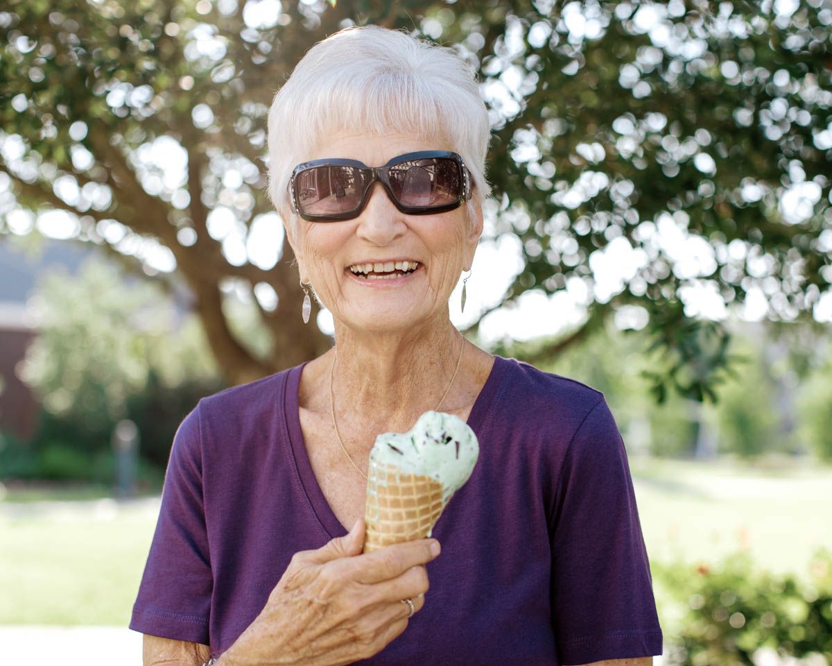Smiling senior woman enjoying an ice cream cone outdoors on a sunny day.