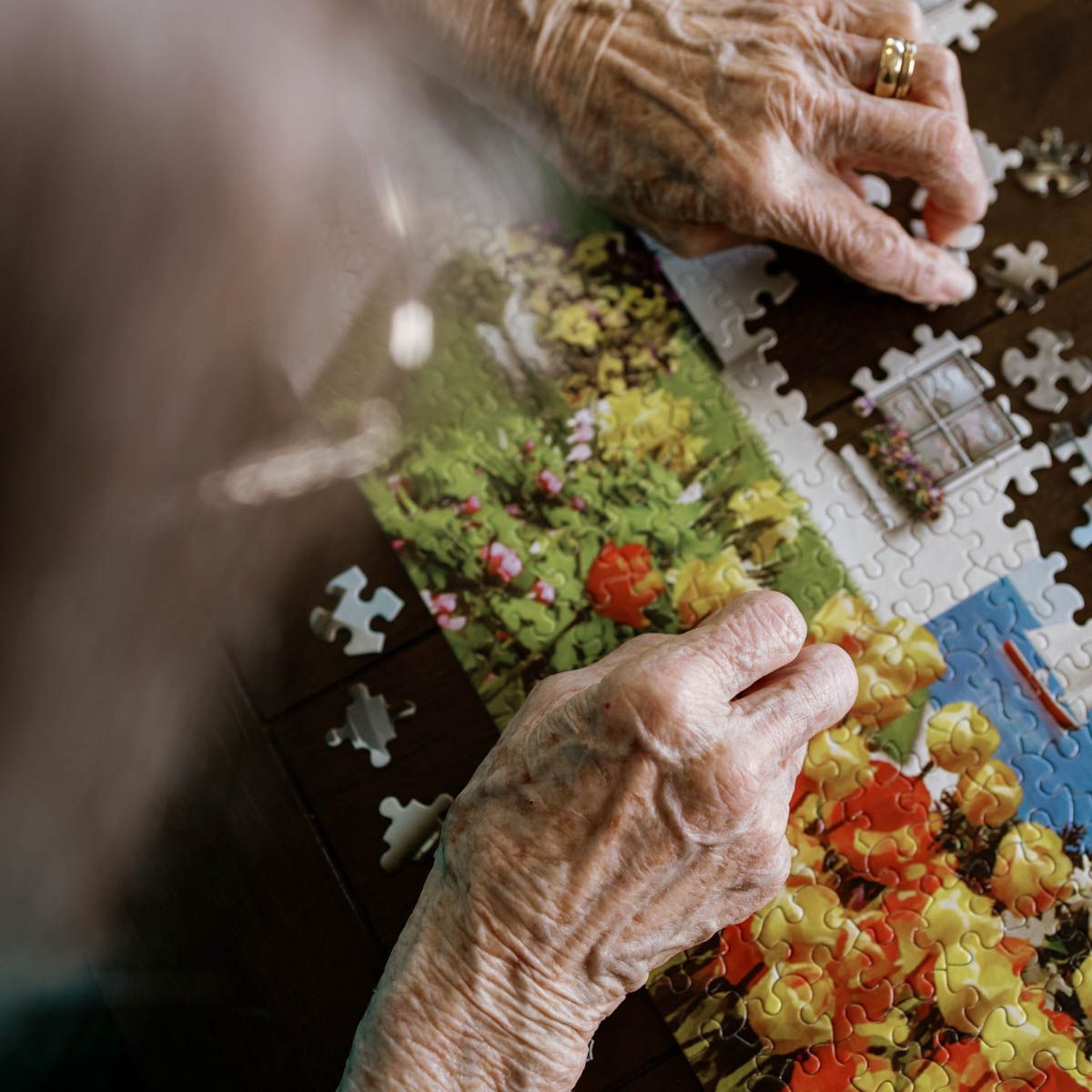 Elderly hands working on a colorful jigsaw puzzle on a wooden table indoors.