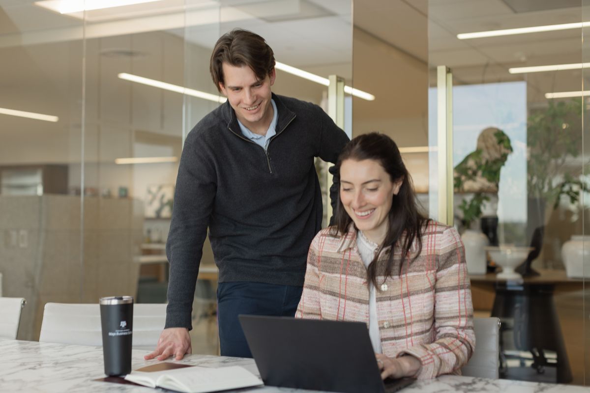 Two colleagues collaborating over laptop and documents at modern office conference table.