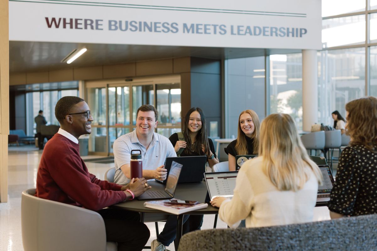 Diverse students collaborate at Texas A&M Mays Business School under a Where Business Meets Leadership sign.