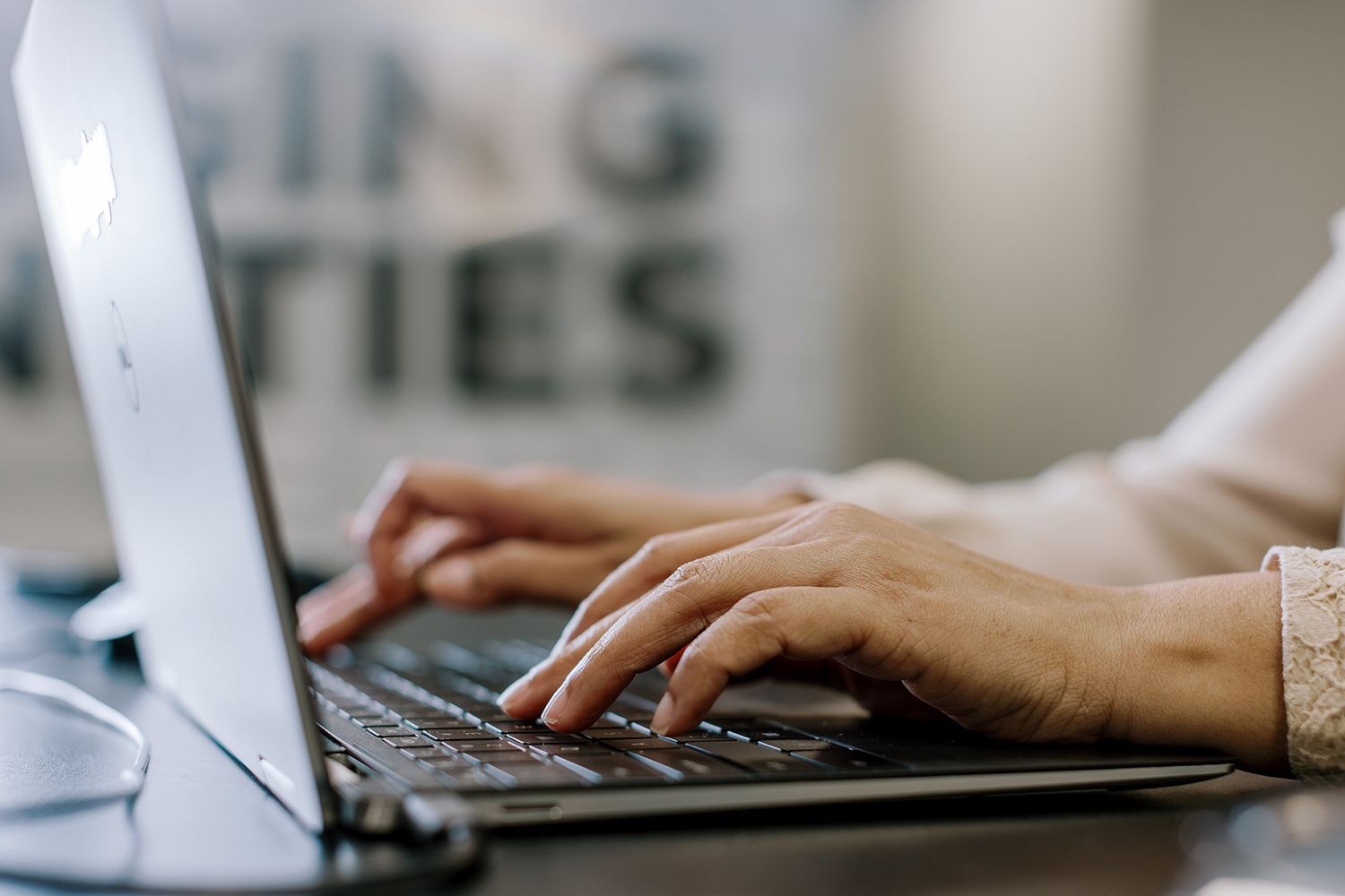 Close-up of hands typing on a laptop keyboard in a modern office setting.