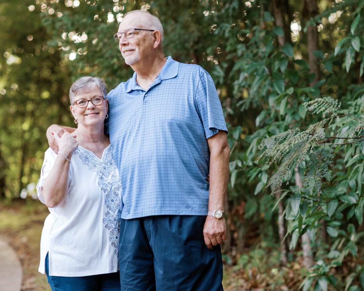 Happy senior couple embracing outdoors surrounded by lush green trees.