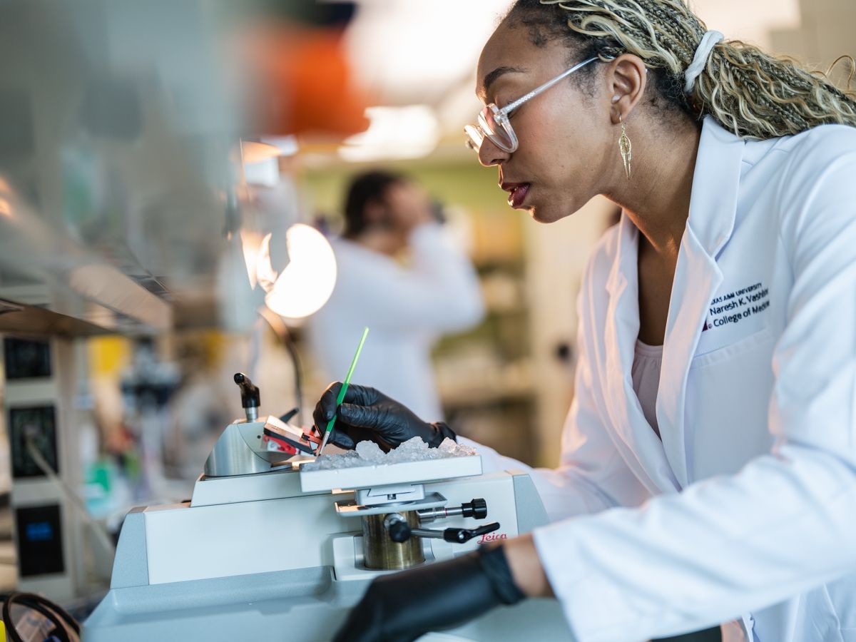 A focused female researcher in a white lab coat works carefully with laboratory equipment.