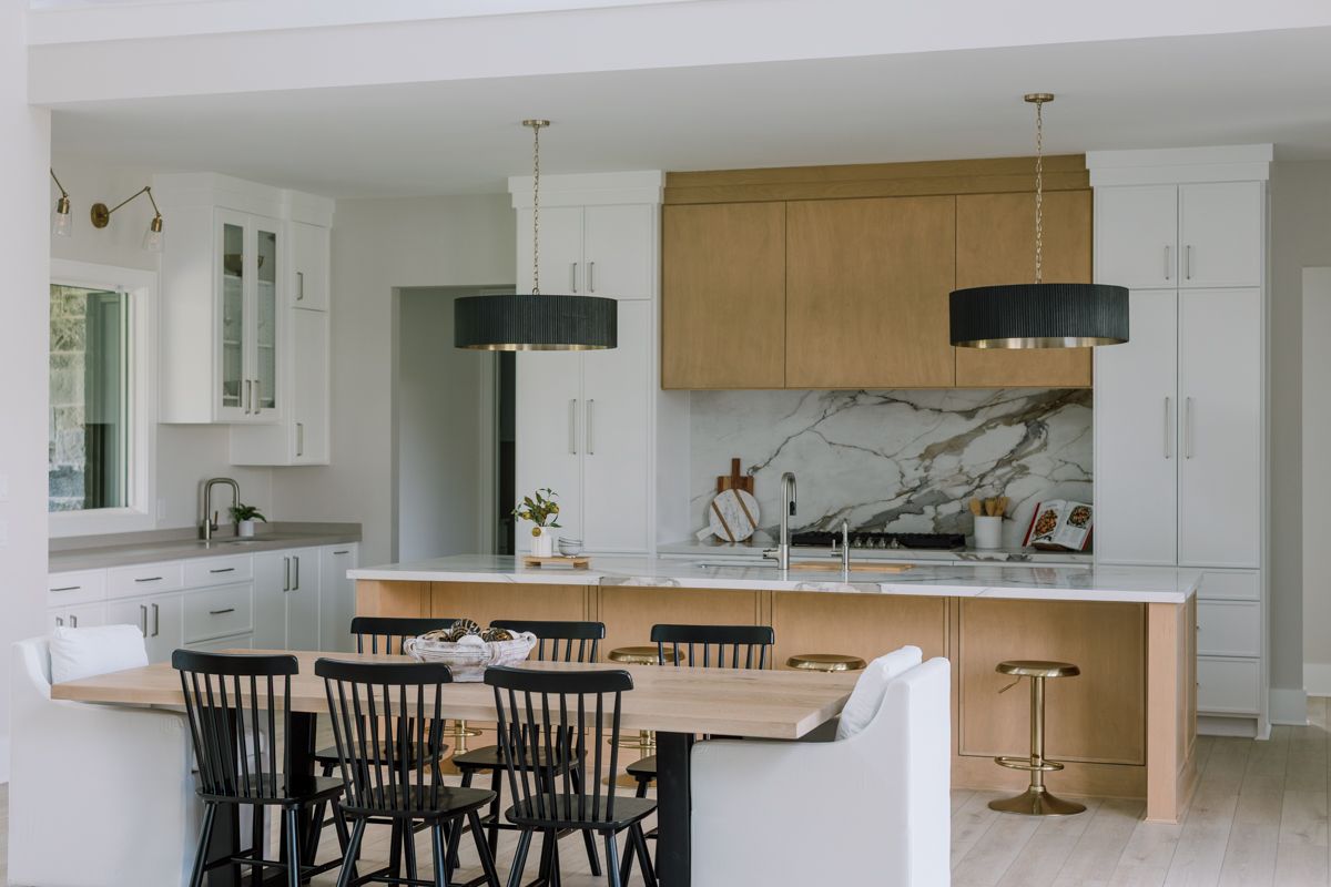Modern kitchen with white and natural wood cabinets, marble backsplash, black pendant lights, and dining banquette.
