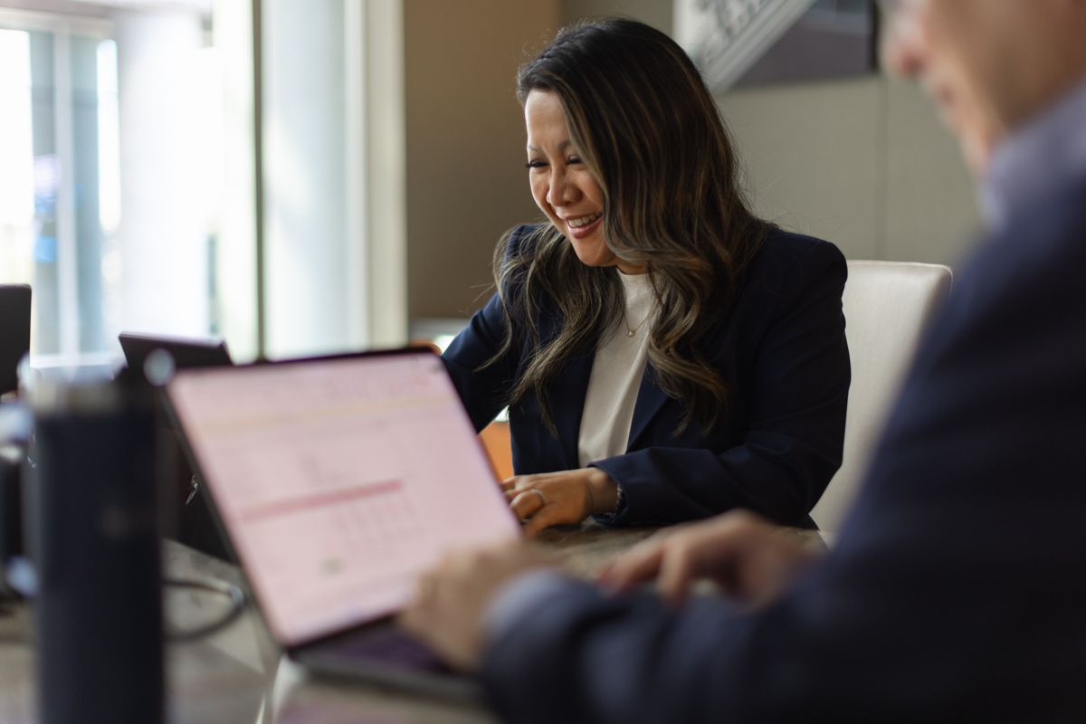 Professional Asian businesswoman smiling while working on laptop in modern office environment.
