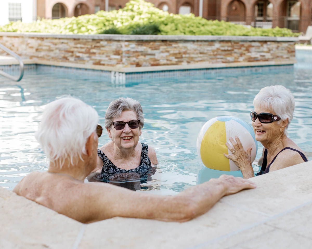 Senior friends enjoying pool time with a beach ball at an outdoor swimming pool on a sunny day.