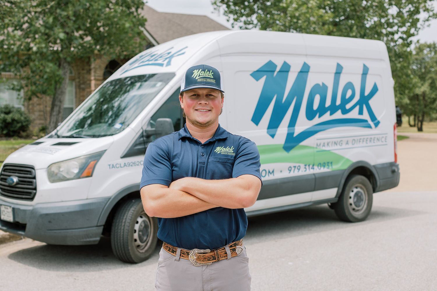 Malek plumbing and heating technician stands confidently with arms crossed in front of a branded company service van.