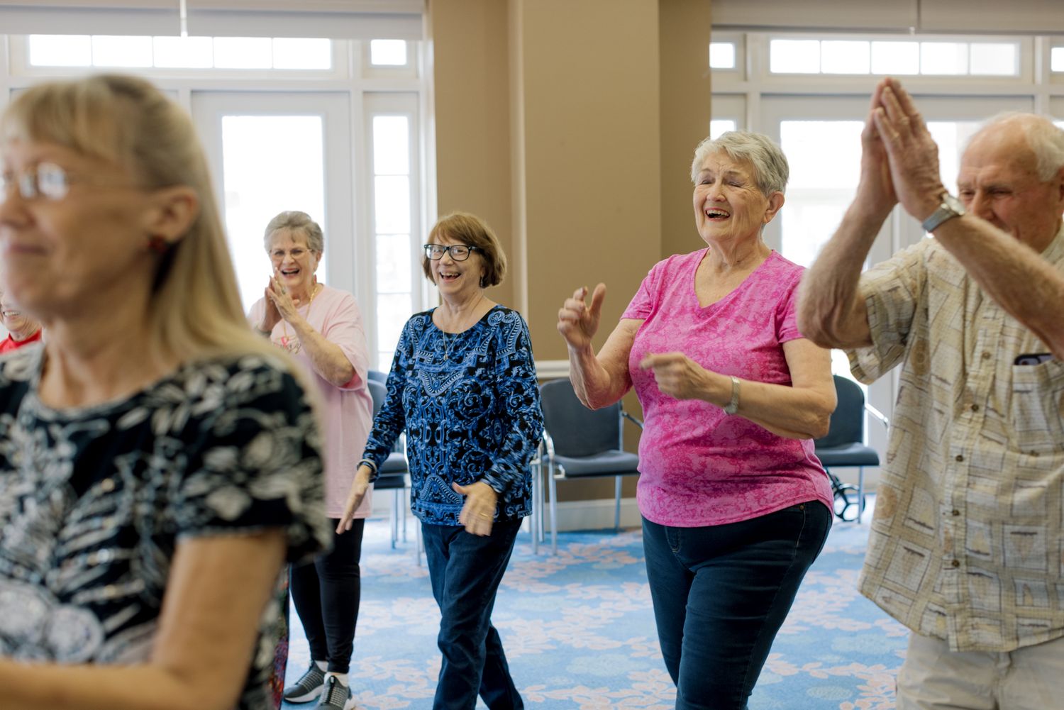 Senior residents enjoying a lively group dance fitness class in a bright community activity room.