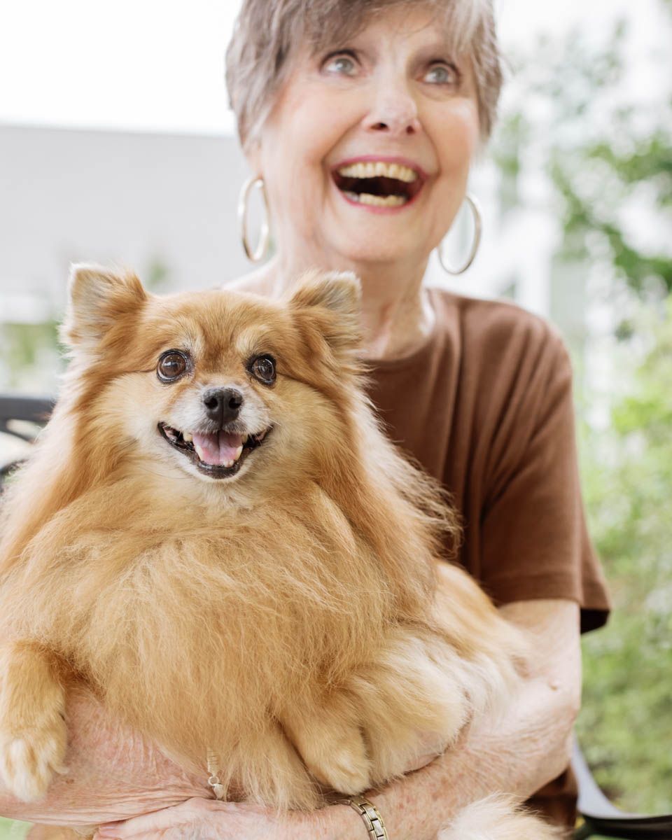Happy senior woman laughing while holding a fluffy golden Pomeranian dog outdoors.