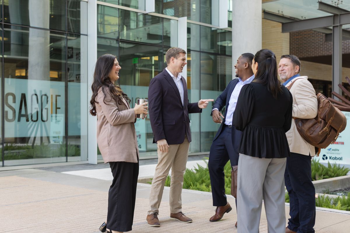 Diverse group of business professionals networking outside a modern glass office building.