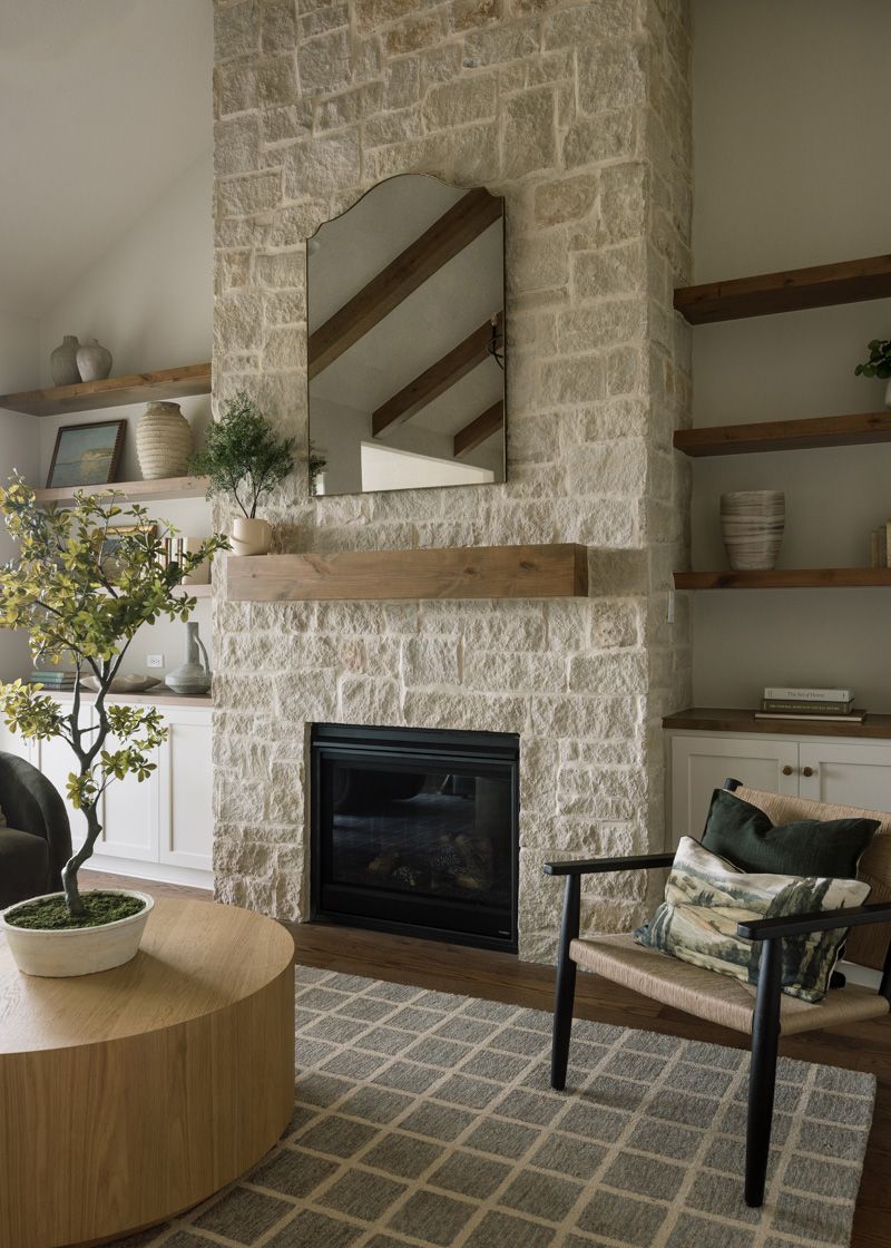 Stone fireplace with wood mantel, arched mirror, flanking open shelves, and vaulted ceiling in a cozy living room.