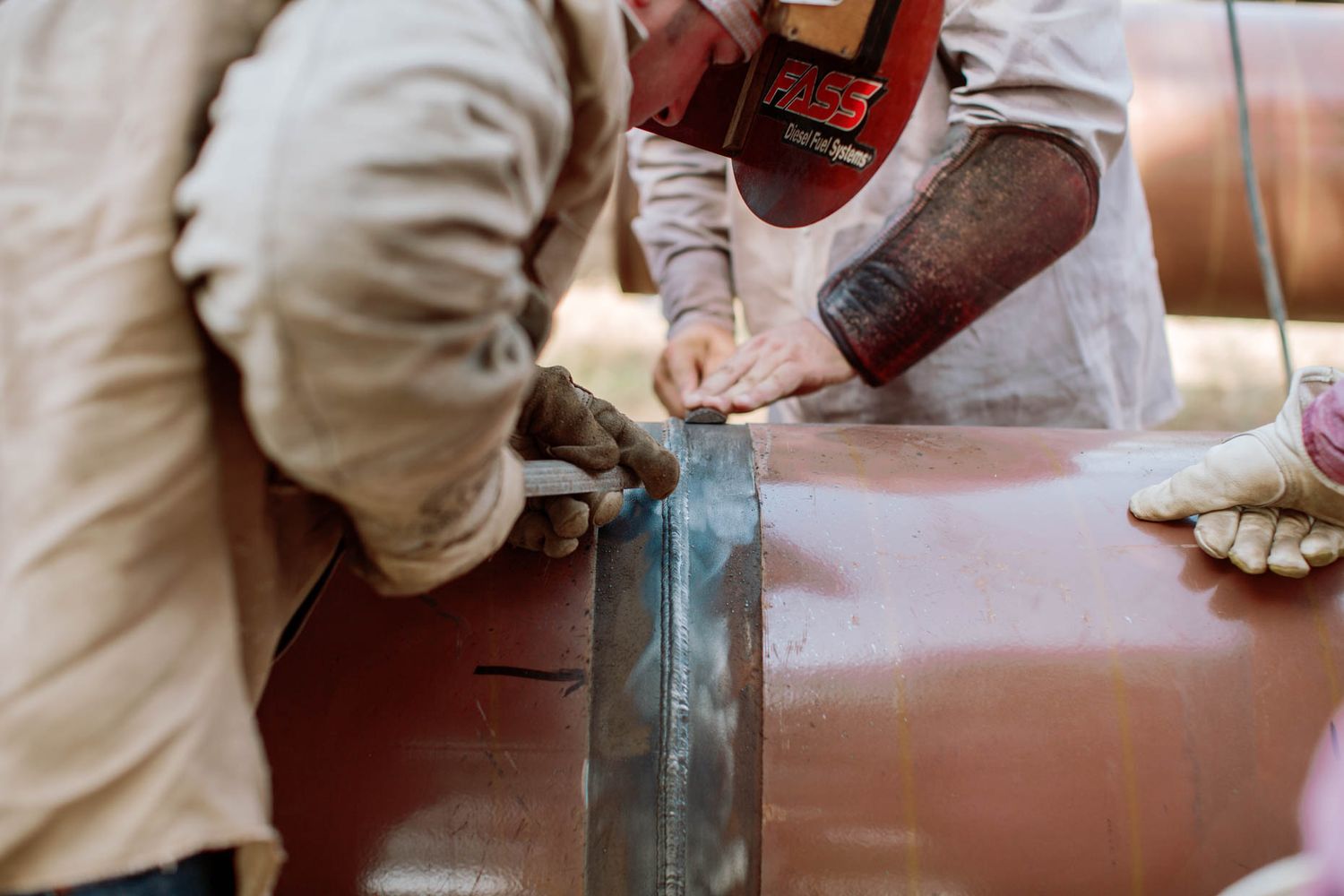 Worker grinding a metal pipe seam with an angle grinder during pipeline construction.