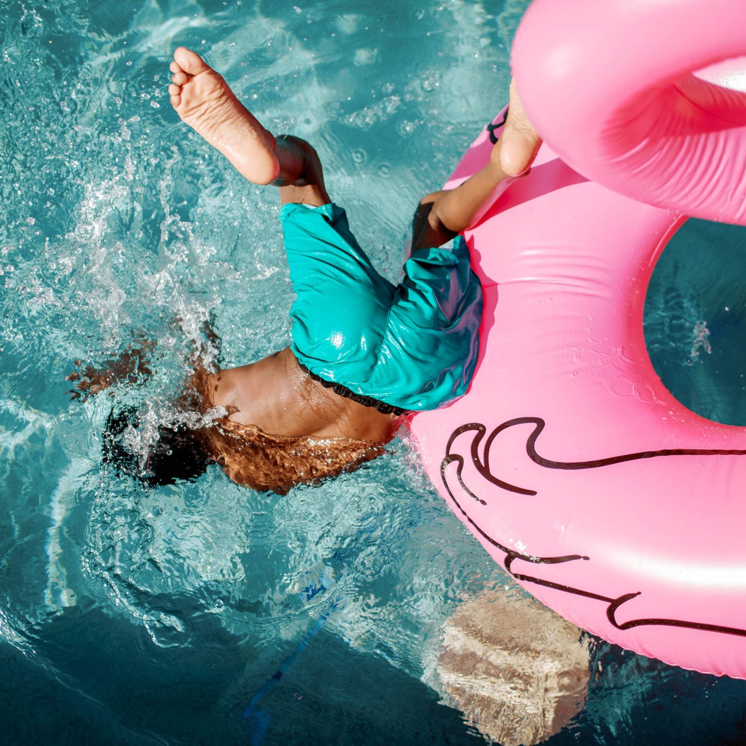 Child diving headfirst into a pool beside a pink flamingo inflatable float on a sunny day.
