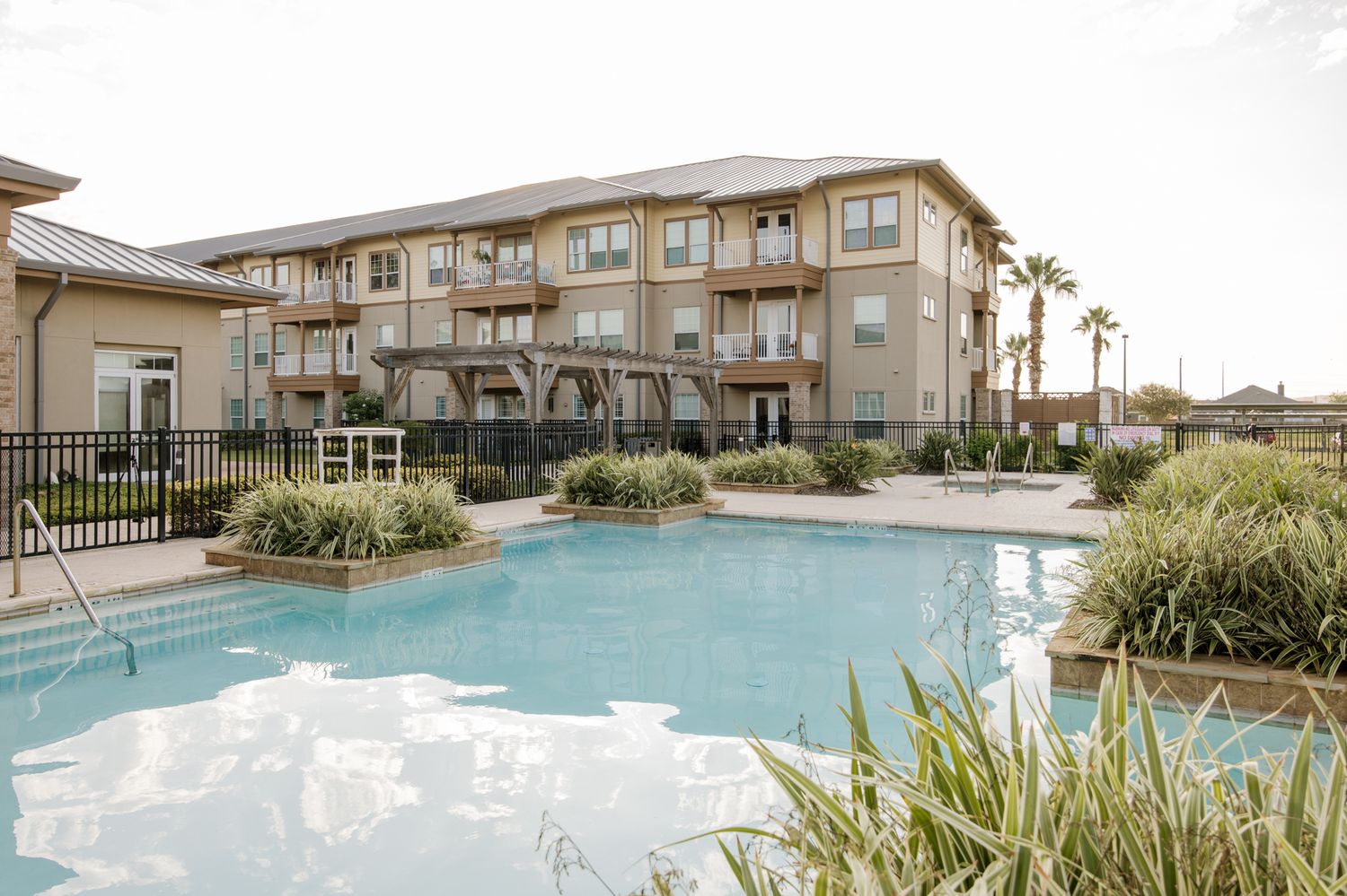 Luxury apartment complex with a sparkling outdoor pool, lush landscaping, and multi-story building with balconies.