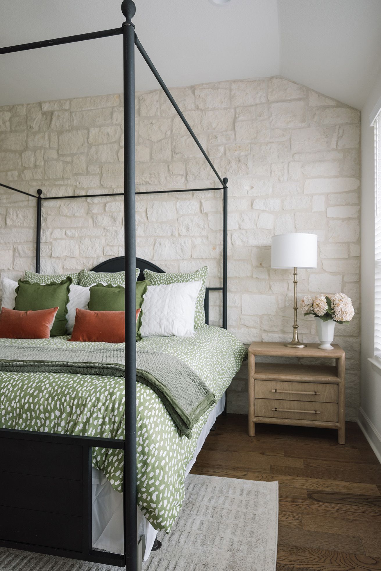 Black four-poster bed with green leopard print bedding against a textured white stone wall in a cozy bedroom.