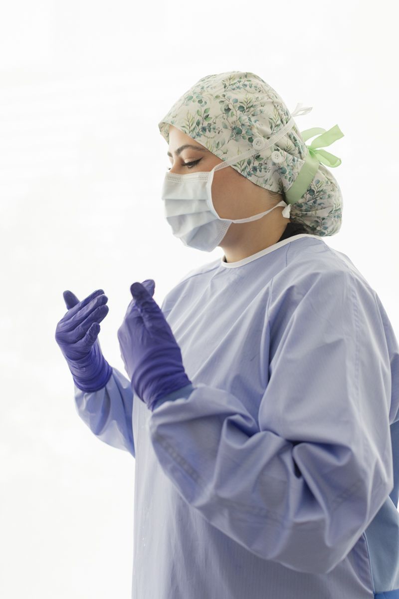 A female surgeon in scrubs, mask, and cap puts on purple sterile gloves before a procedure.