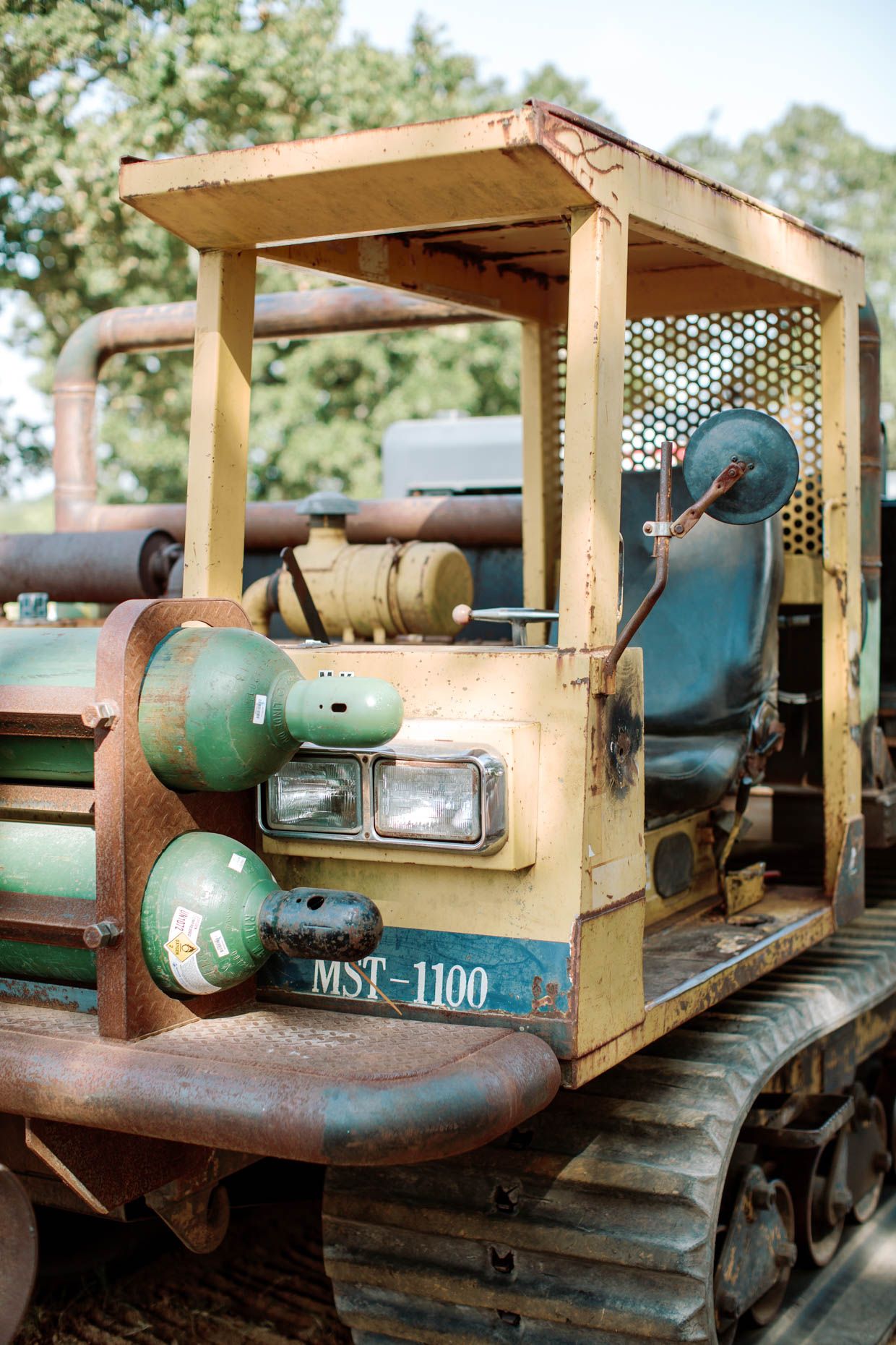 Rusty MST-1100 tracked crawler machine with yellow cab frame and green components outdoors.