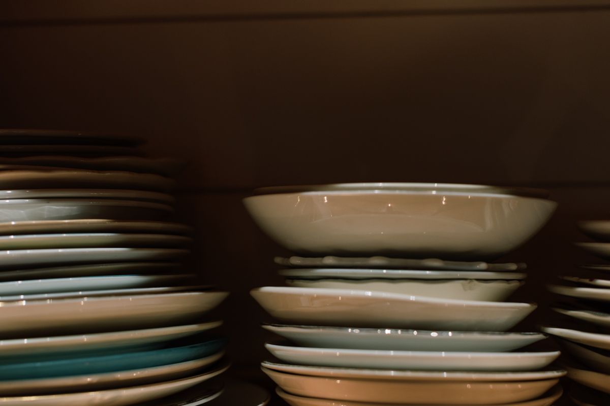 Stacks of assorted ceramic plates on dark wooden shelves in a restaurant.