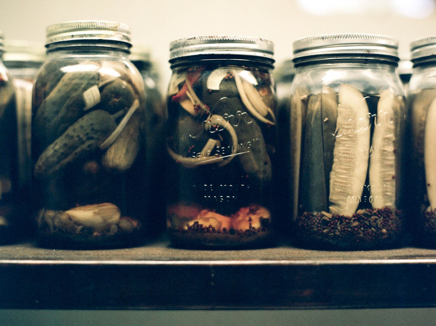 Three mason jars filled with pickled vegetables on a wooden shelf in a dimly lit setting.