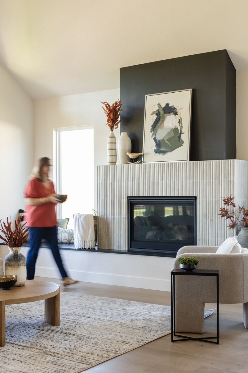 Contemporary living room with fluted tile fireplace, dark accent wall, abstract art, and blurred figure in motion.