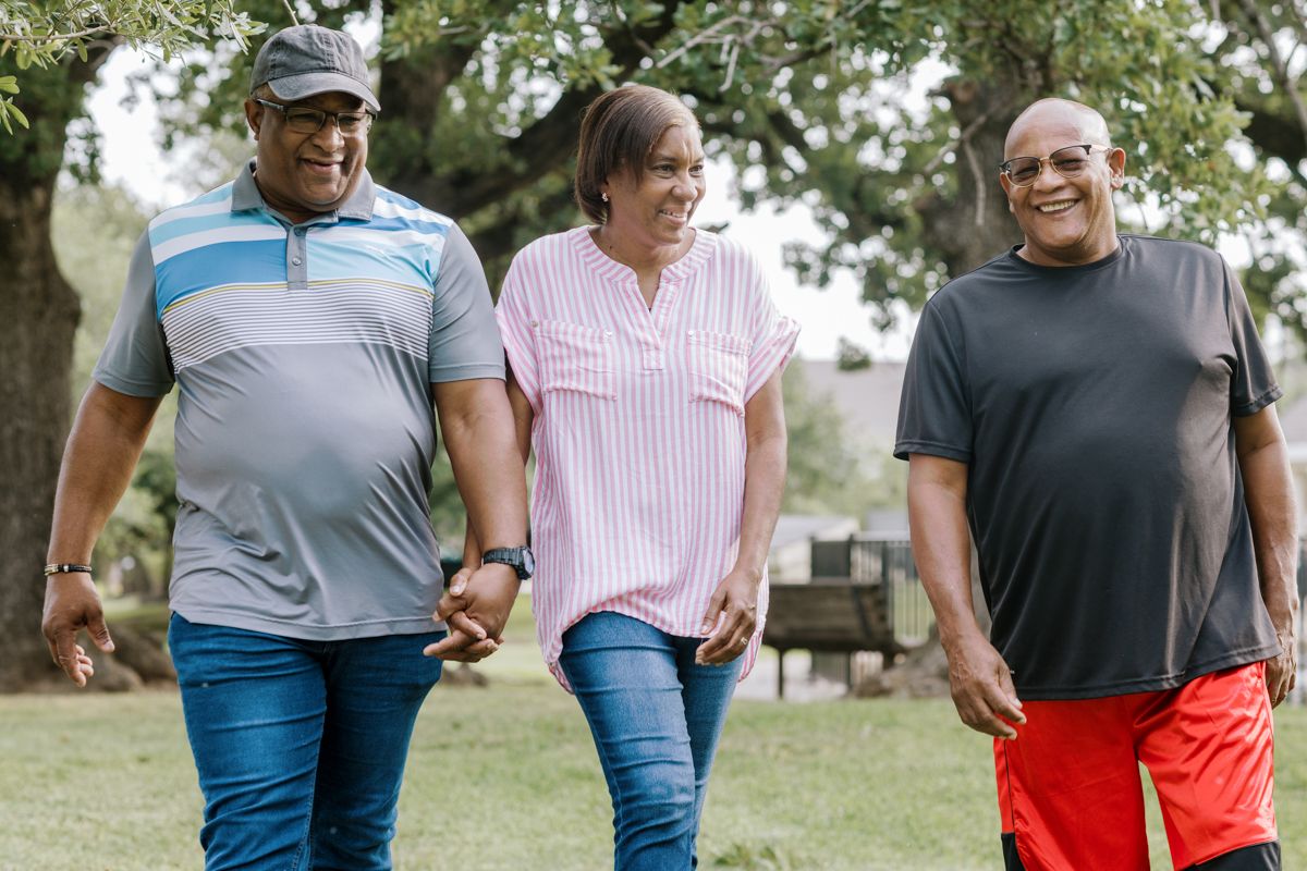 Three middle-aged adults walking together and smiling in a park on a sunny day.