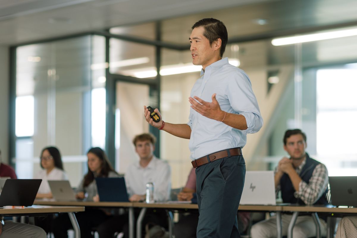 Young man presenting to a group of students in a modern classroom setting.