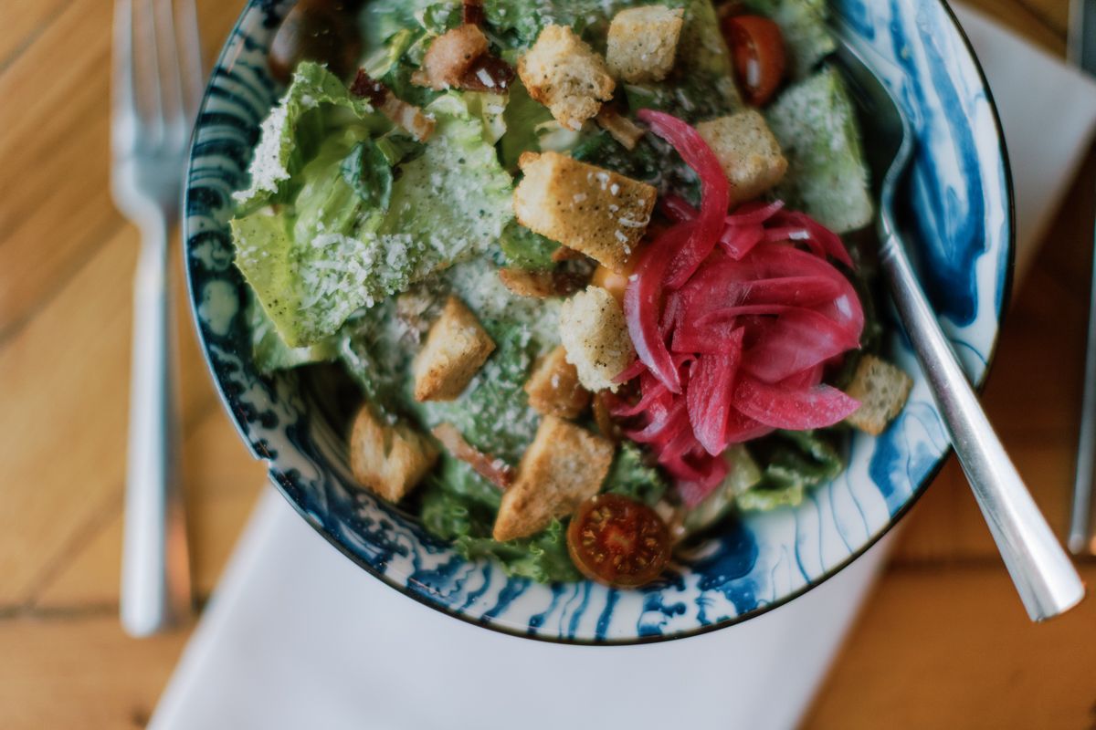 Fresh Caesar salad with croutons, pickled onions, and cherry tomatoes in a blue ceramic bowl.
