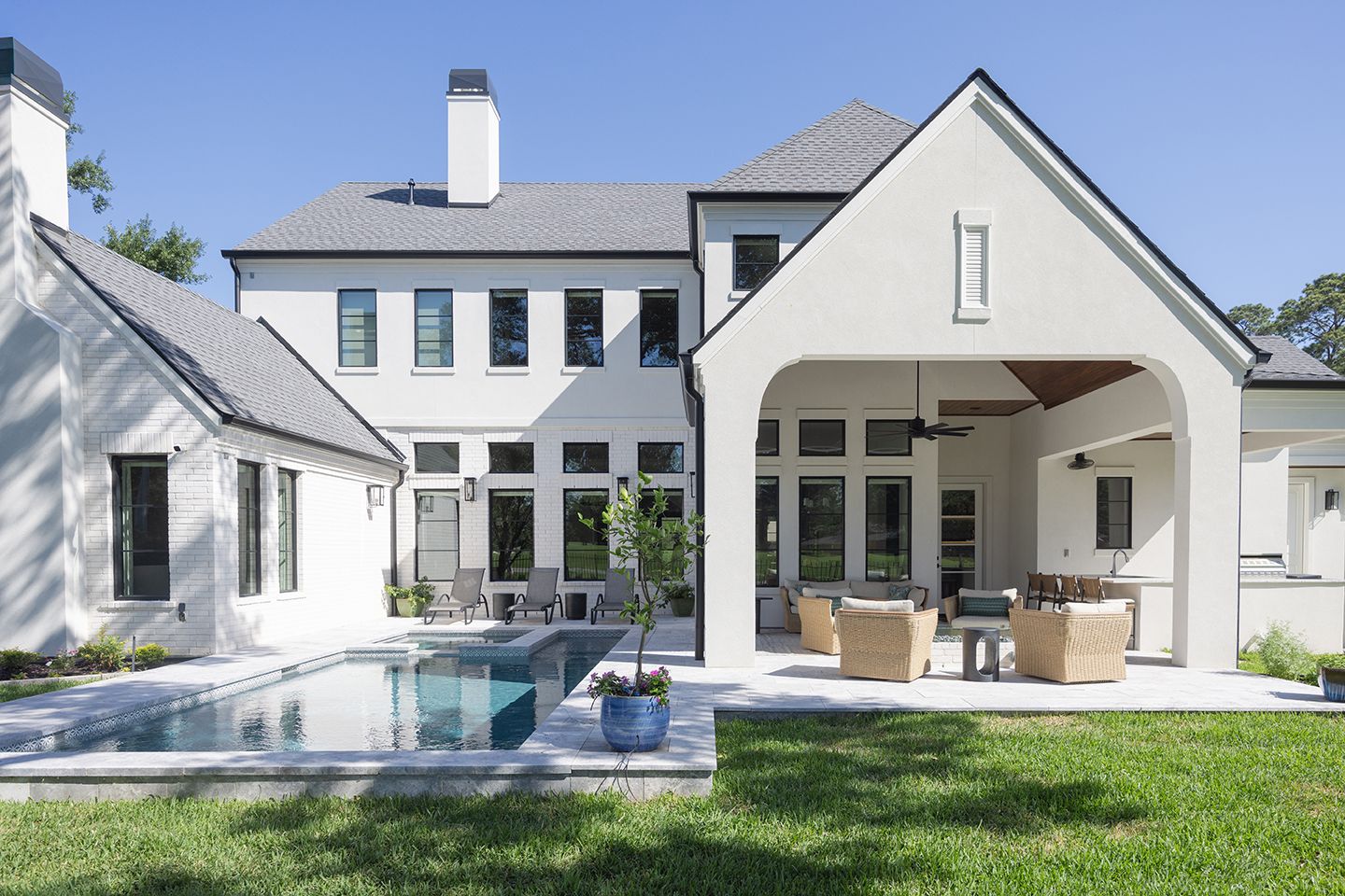 White modern farmhouse exterior with black windows, covered patio, pool, and lush green lawn.