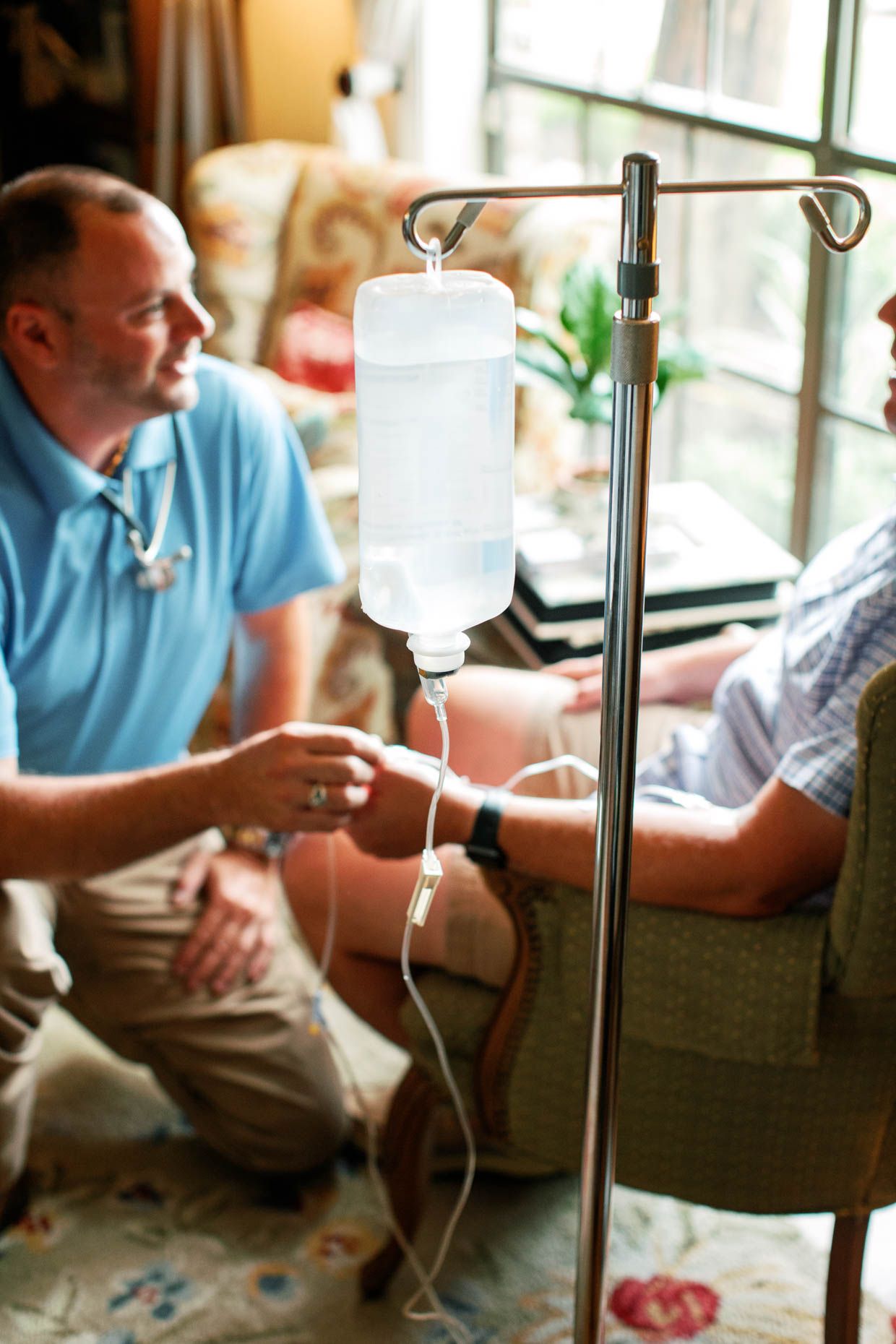 A male nurse administers an IV drip to a patient at home during a house call visit.