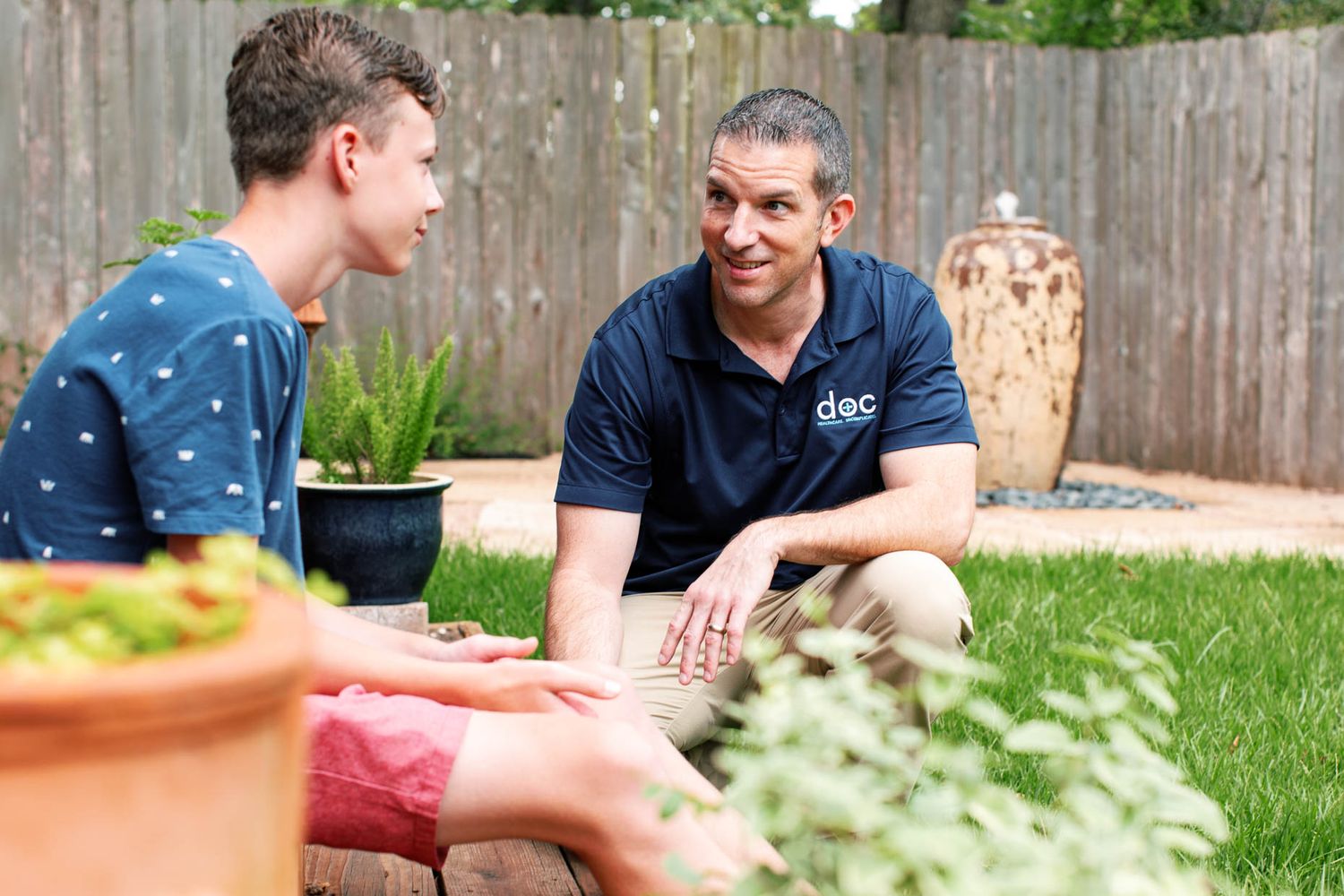 Two men having a friendly conversation while sitting in a backyard garden patio area.