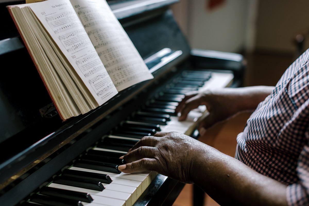 Elderly hands playing piano keys with open sheet music on a dark upright piano.