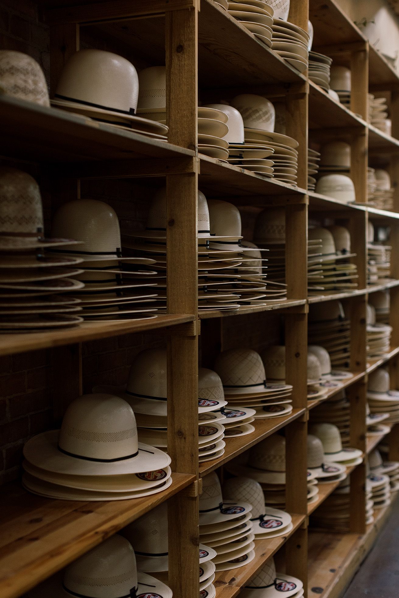 Wooden shelves stacked with various white and cream hats in a hat shop or factory storage room.
