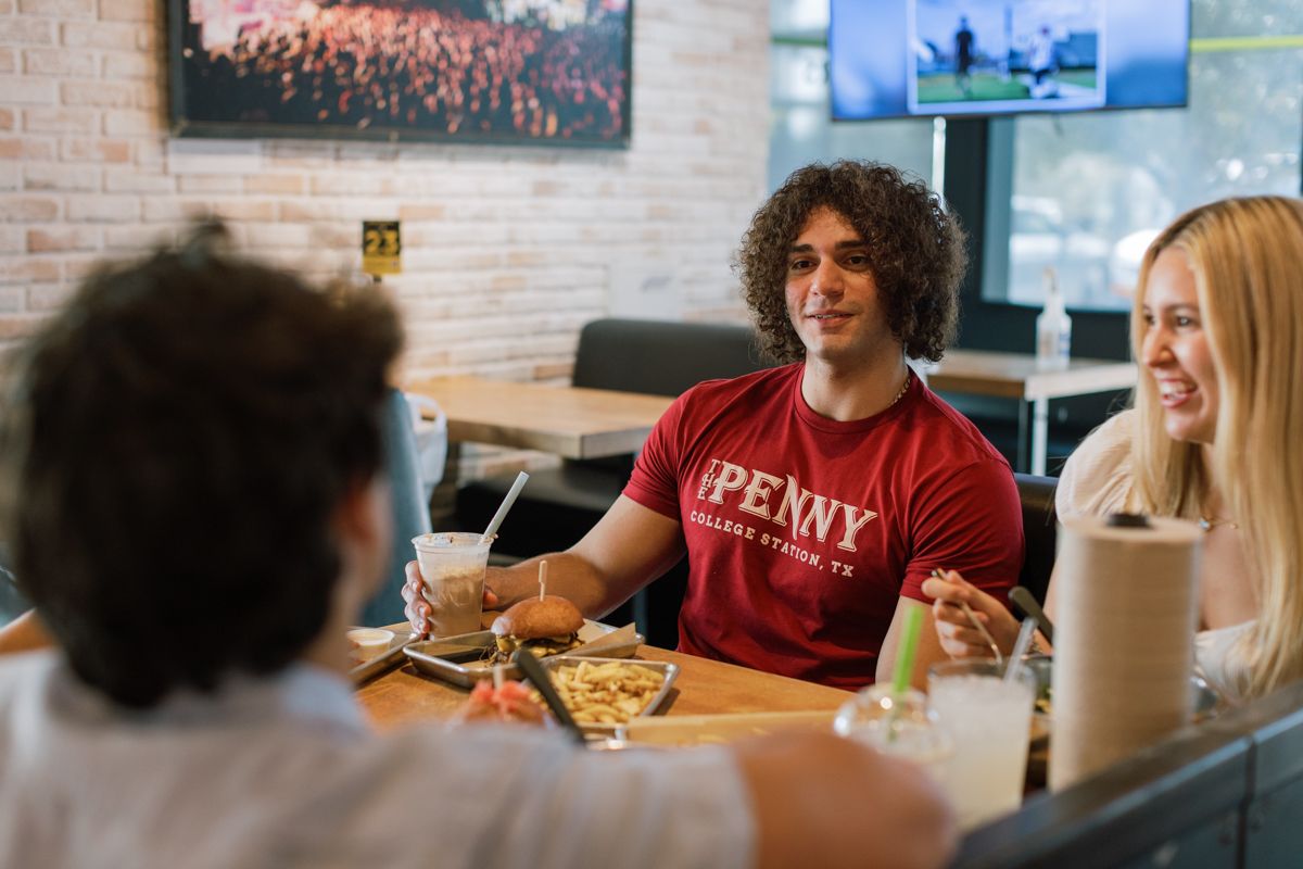 Three young adults enjoying pizza and drinks together at a casual restaurant booth, smiling and laughing.