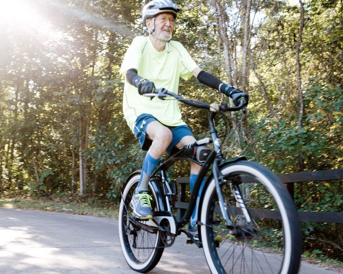 Active senior man riding a mountain bike on a paved trail through the woods.