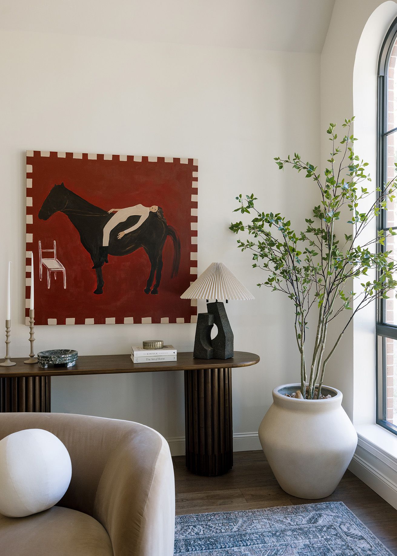 Elegant corner vignette with bold equestrian artwork, fluted console table, and tall olive tree.