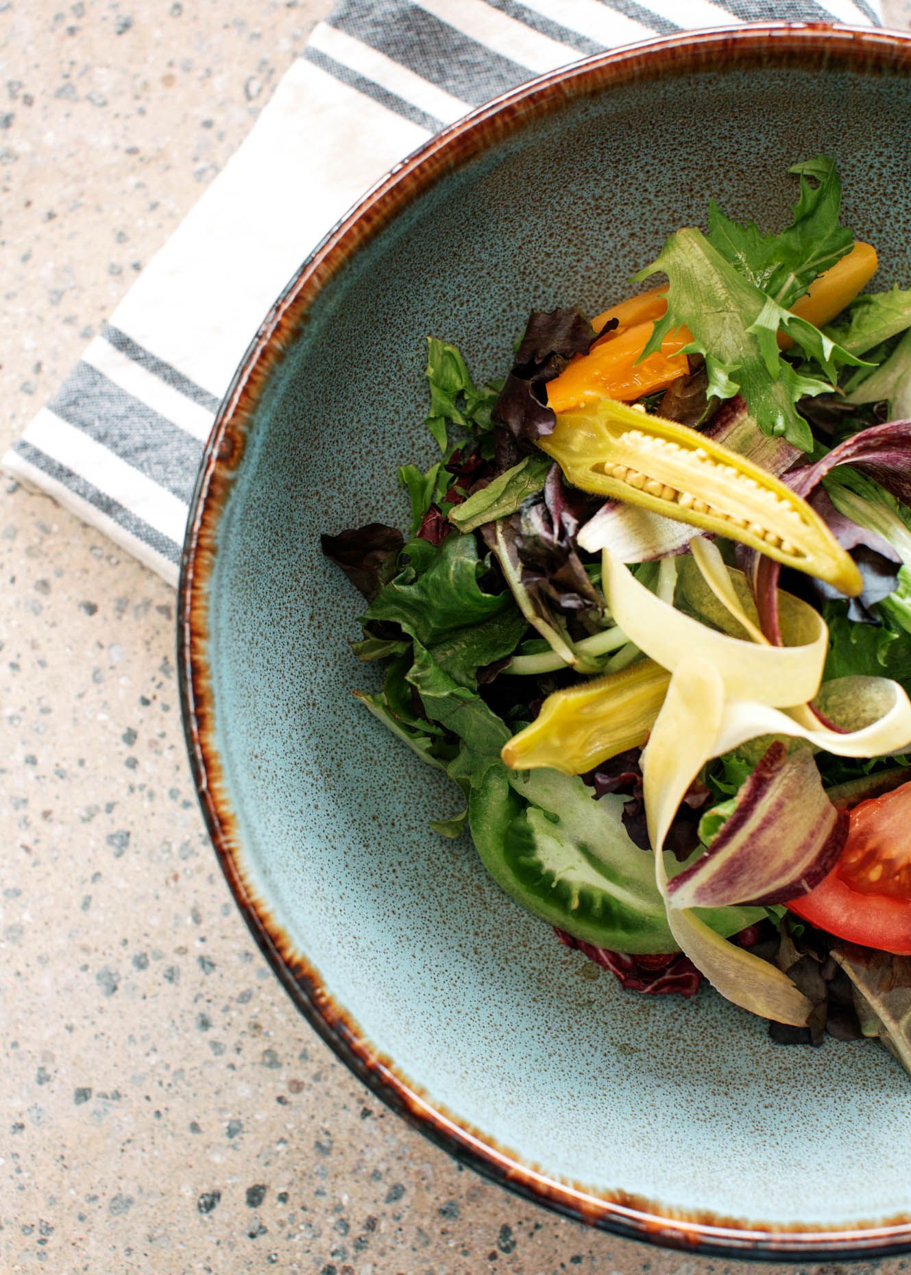 Fresh mixed greens salad with colorful vegetables served in a rustic ceramic bowl on a terrazzo surface.
