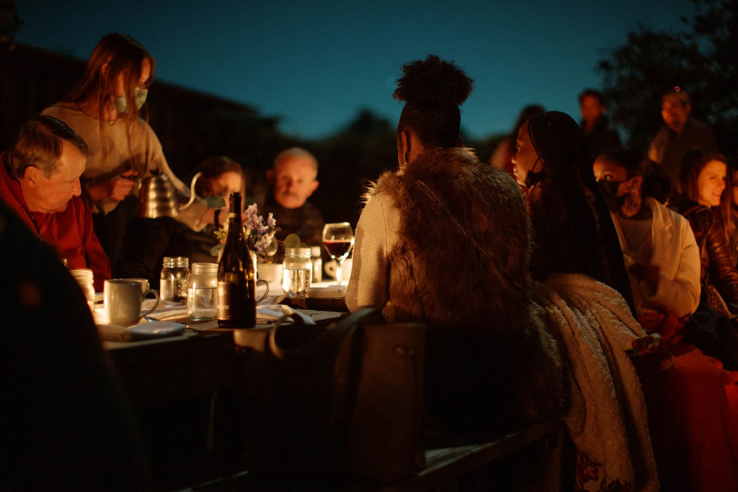 Guests gathered around a candlelit outdoor dinner table at dusk, enjoying an intimate evening dining experience.