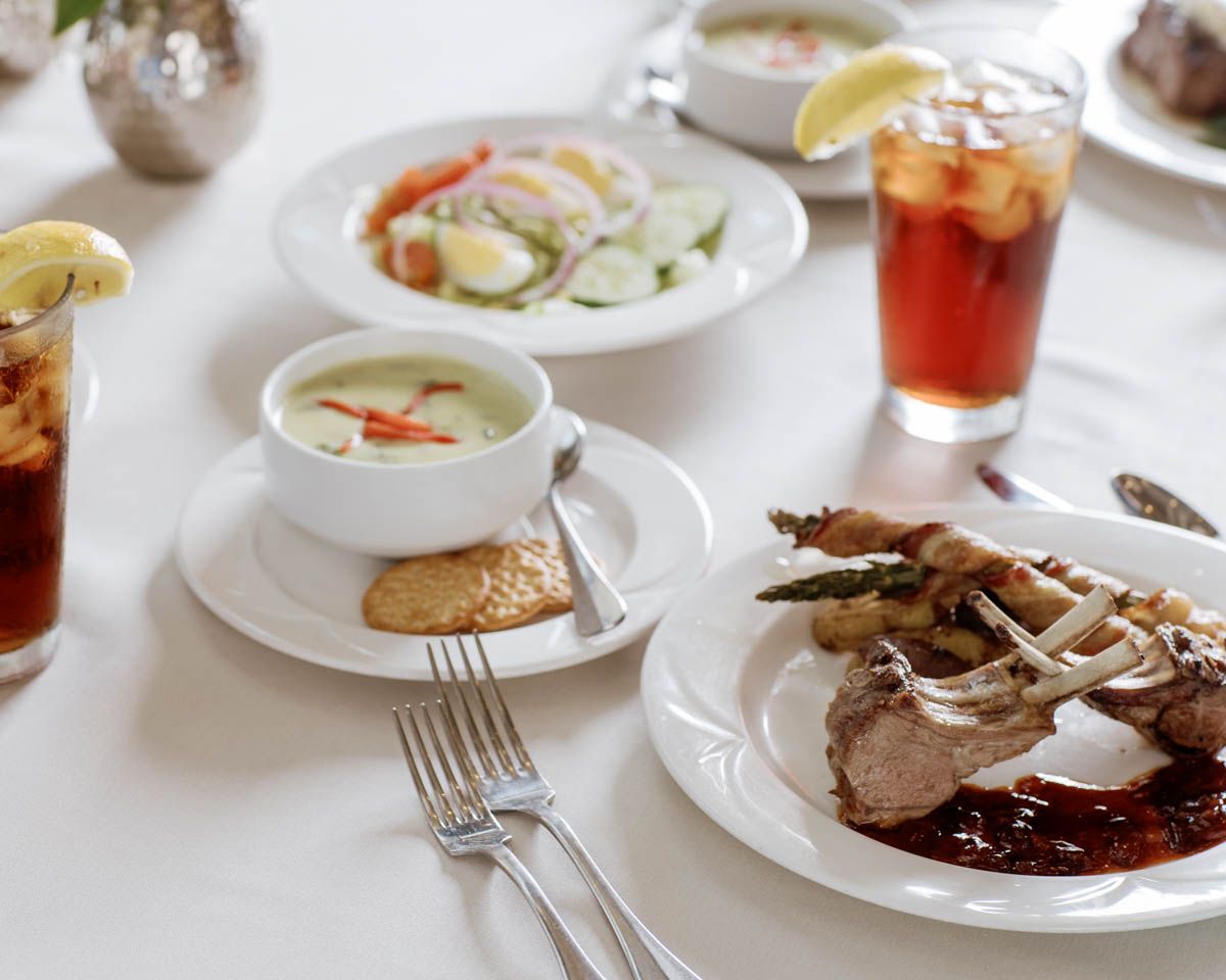 Elegant senior dining table with gourmet dishes, iced tea, soup, and plated entrees on white linen.