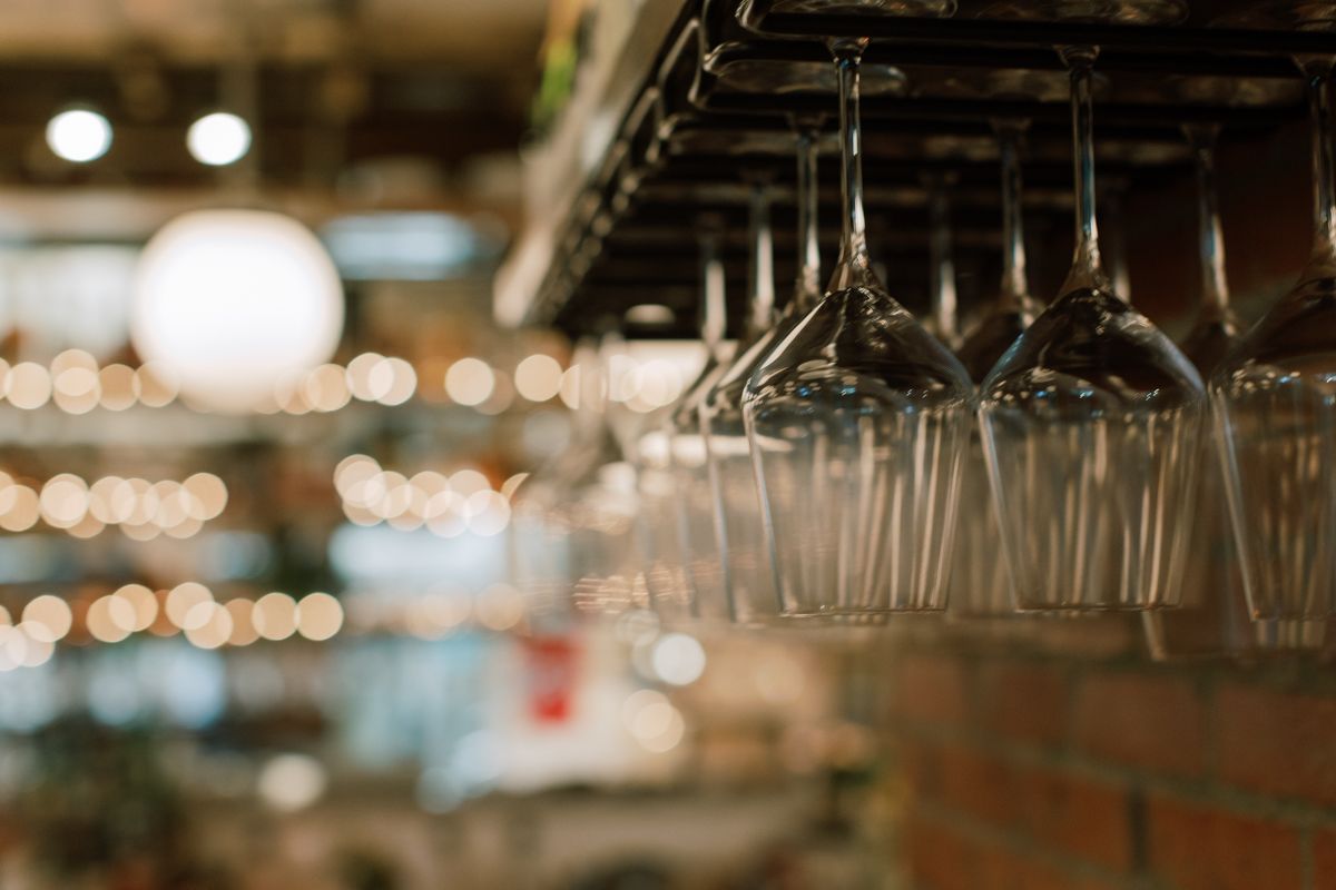 Empty wine glasses hanging upside down on a rack above a blurred restaurant bar background.