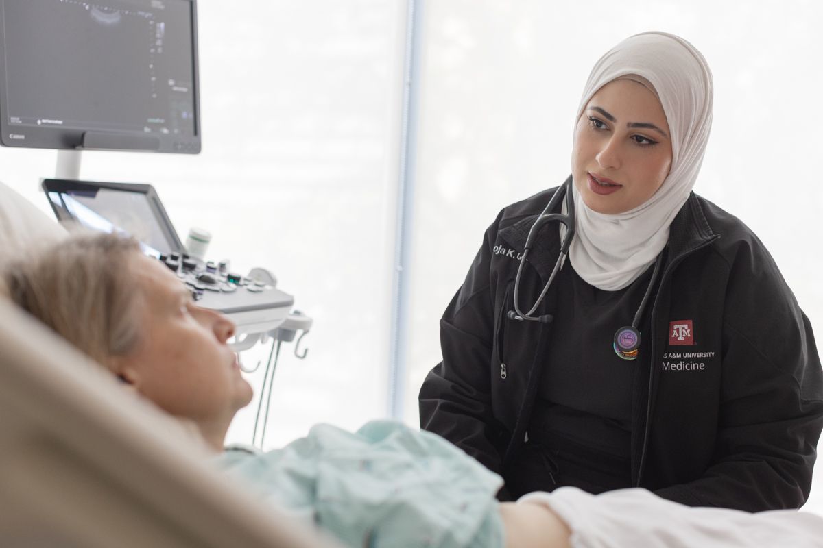 A medical professional in hijab consults with a patient lying in a hospital bed near an ultrasound machine.