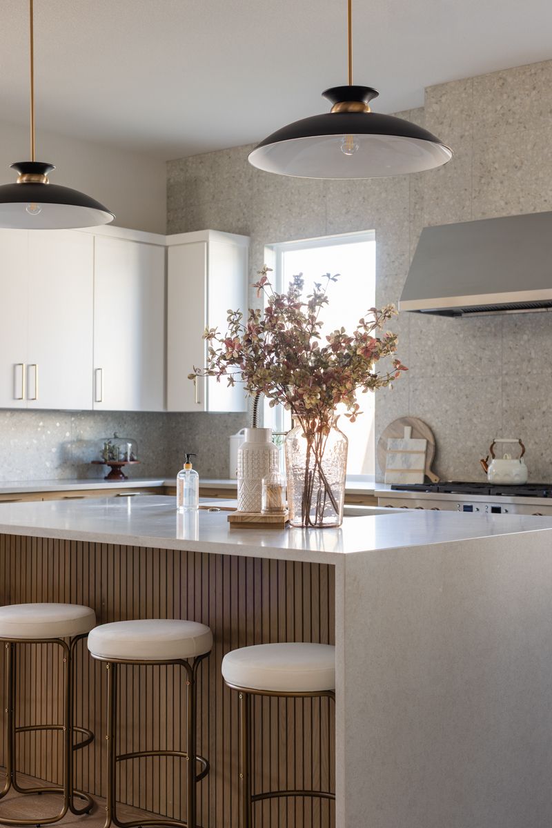 Modern kitchen with white cabinets, fluted island panels, terrazzo backsplash, black dome pendants, and fresh floral arrangement.
