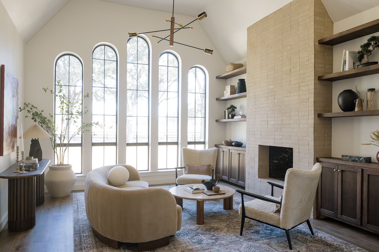 Airy living room with arched windows, curved cream sofas, stone fireplace, and built-in shelving.