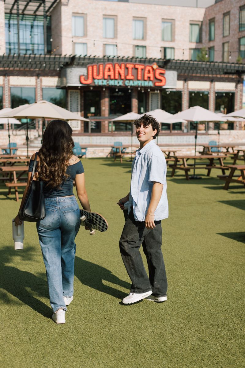 Two friends walk on green grass outside Juanita's Tex-Mex Cantina on a sunny day.