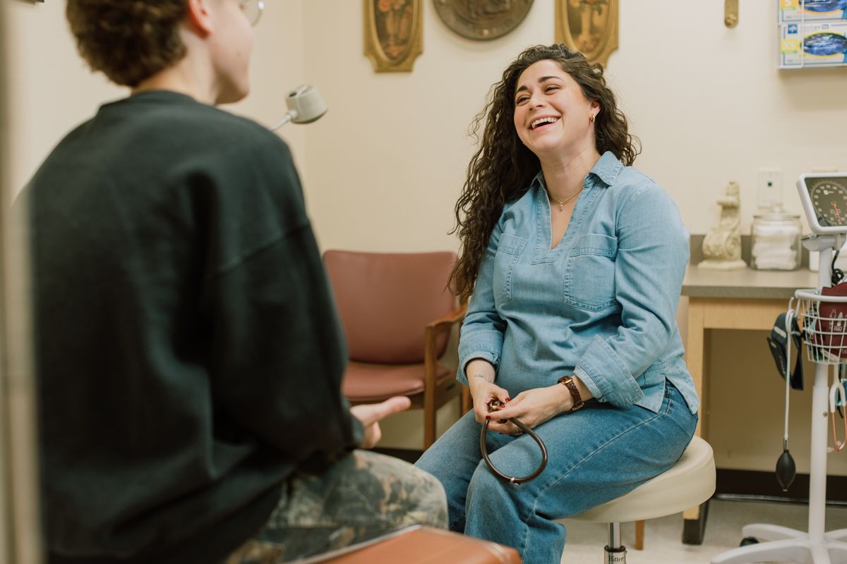 A female medical professional laughs while holding a stethoscope during a patient consultation.