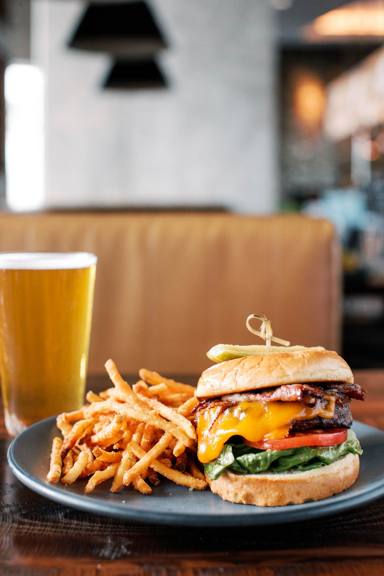 A juicy bacon cheeseburger with fries on a dark plate, served with a cold draft beer in a restaurant.