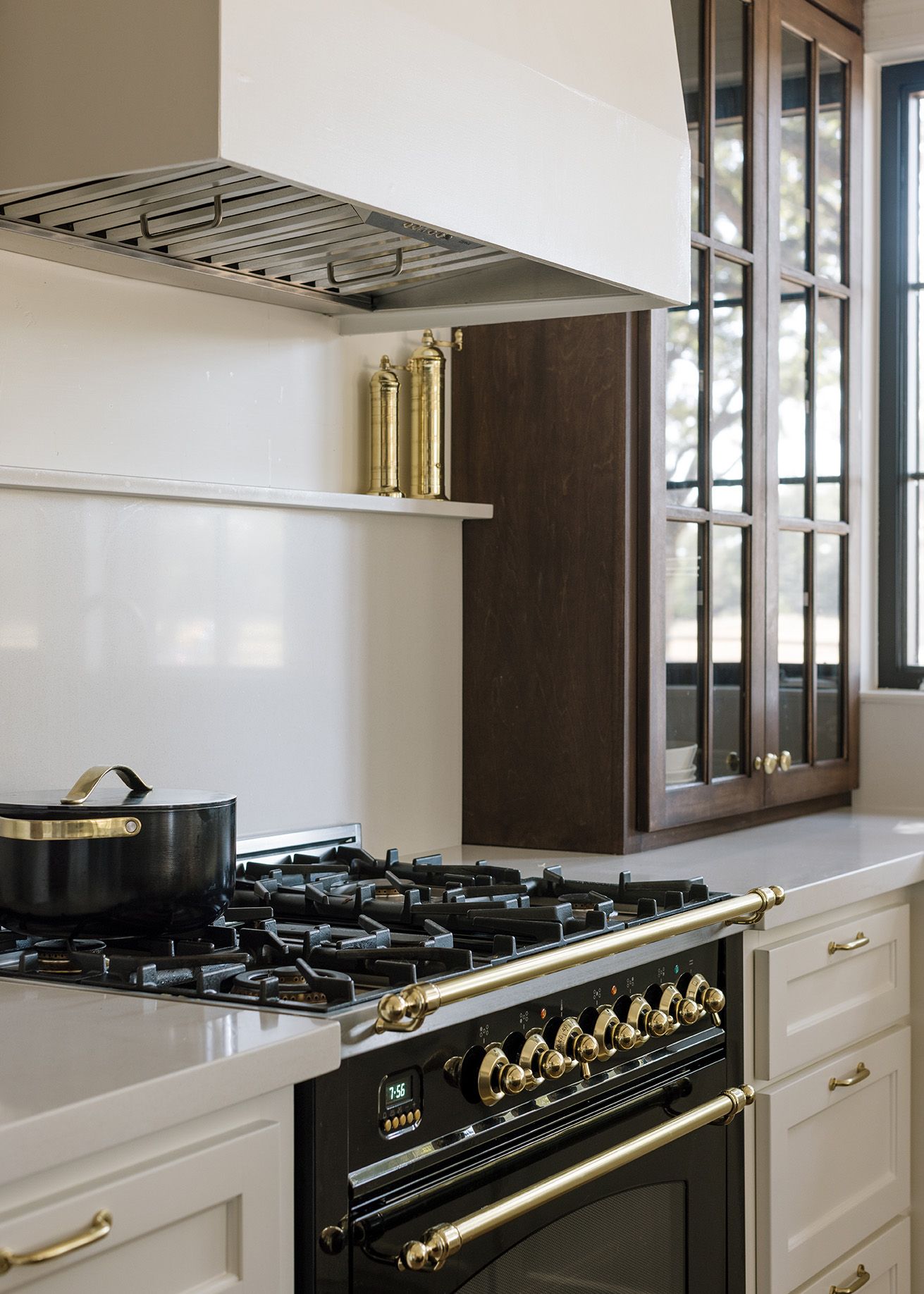 Luxury kitchen featuring black and gold range, white hood, and dark wood glass-front upper cabinets.