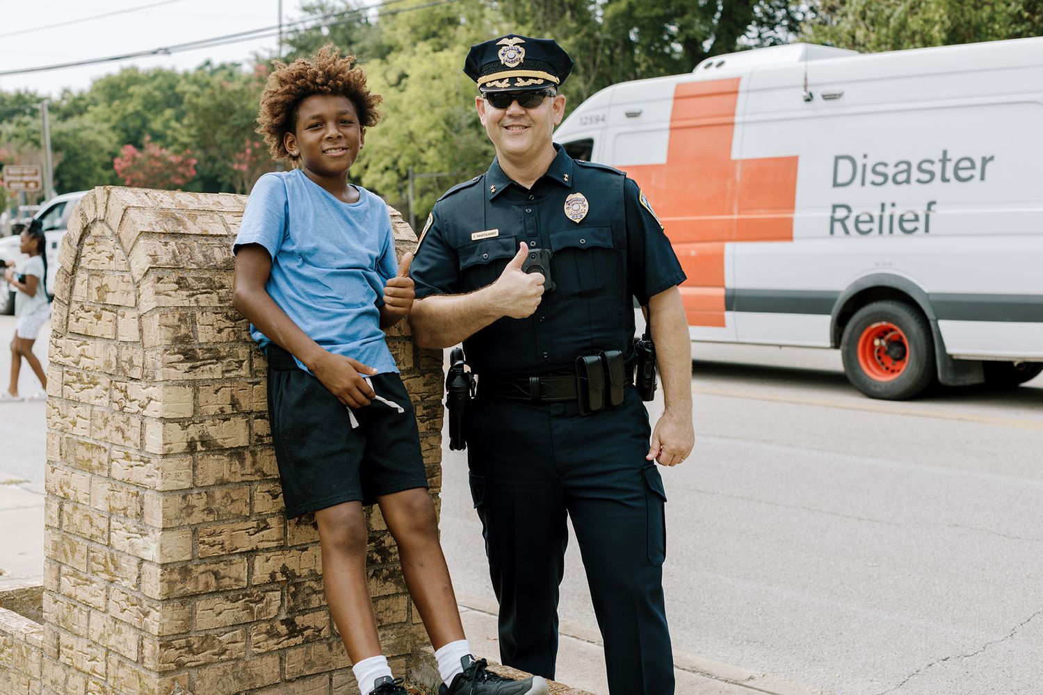 Police officer and child pose together near Disaster Relief van outdoors.